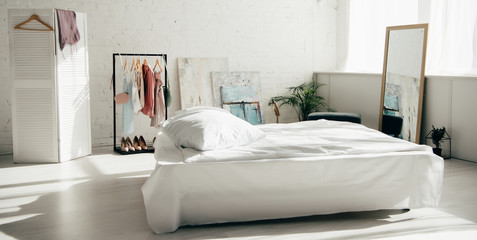 panoramic shot of modern white bedroom with bed and wardrobe