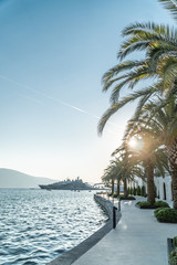 Pier near the sea in a European resort town with palm trees on the shore and the mountain and yachts in the background. Vertical shot