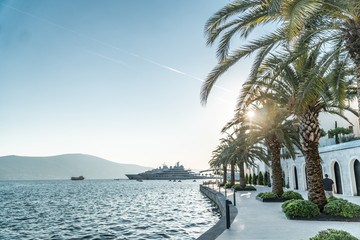 Pier near the sea in a European resort town with palm trees on the shore and the mountain and yachts in the background. Horizontal shot