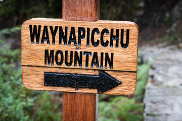 Closeup of wooden pointing sign with black label to Waynapicchu mountain coved with drops