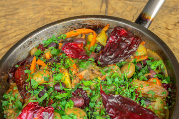 Vegetables roasted on a pan. Dried red peppers, eggplant, carrots, onion, garlic, potatoes, black and green olives and spices. Sprinkled with fresh parsley. Closeup.