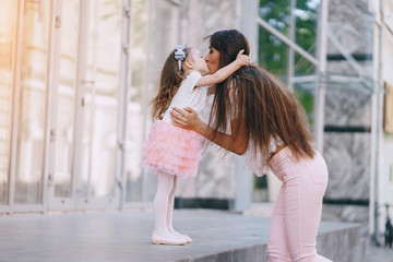 Young and very beautiful slim mum with long hair walking in a sunny summer city with her little beauties daughters