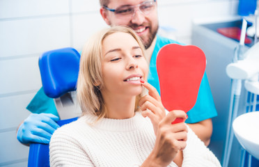 Satisfied blond girl looking in red mirror after dentist's work