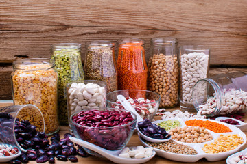 Various legumes: beans, chickpeas, lentils in glass jars on wooden background. Healthy vegetarian...