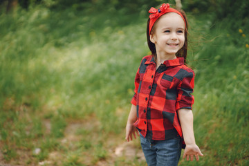 A beautiful little girl in a red shirt and blue pants is walking in the summer forest