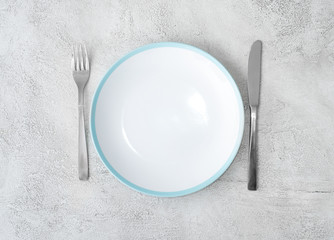Fork,knife and empty white plate with blue border on gray background