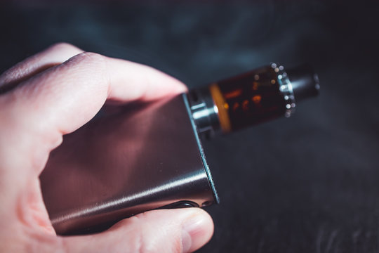 Man holding vape pen metal electronic cigarette with vaping smoke cloud  dark background Stock Photo | Adobe Stock