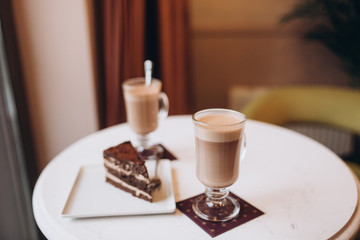Two cups of cappucino with piece of cake in modern cafe