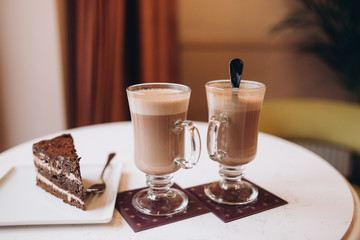 Two cups of cappucino with piece of cake in modern cafe