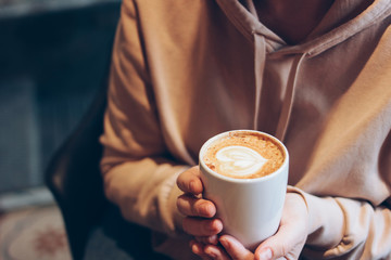 Cup of coffee cappuccino with foam heart in female hands at cafe, close up