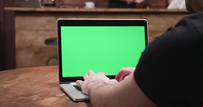 Revealing shot of a man working on a green screen computer in vintage pub or coffee shop