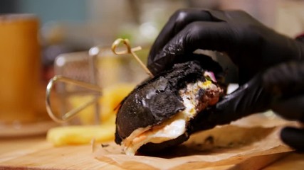 A person taking a black burger in their hands and taking a piece