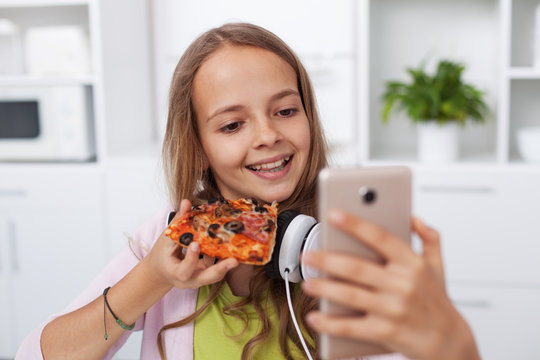 Happy teenager girl taking a selfie in the kitchen posing with a slice of pizza