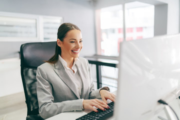 Smiling secretary dressed in formal wear typing on keyboard e-mail while sitting in office. It's not about being the best. It;s about being better than you were yesterday.