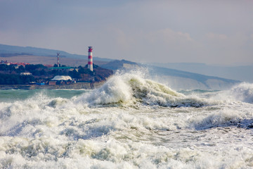 Fototapeta na wymiar Beautiful and dangerous storm waves on the background of the Gelendzhik lighthouse. Resort Gelendzhik, Caucasus, steep rocky shore.
