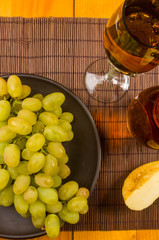 large brush of green grapes in a ceramic plate, a decanter and a glass of wine and cheese