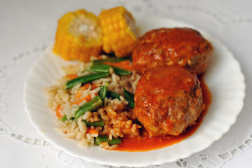 Meat cutlets with tomato sauce, rice and vegetables on a white ceramic plate. Close-up