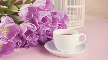 A cup of tea and violet tulips on the table