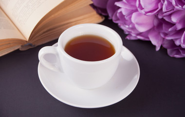 A cup of tea, book and violet tulips on the table