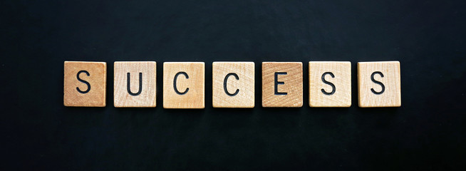 The Word Success is Spelled out in Wooden Blocks on Black Leather Background