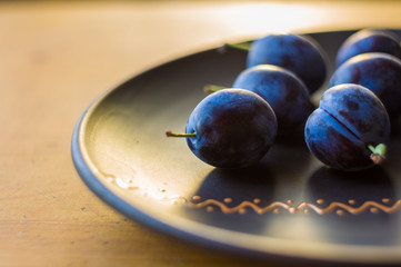juicy blue plums in ceramic plate on wooden background