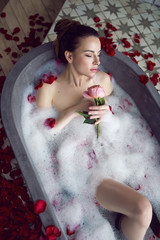 beautiful girl lying in a stone bath with rose petals and foam