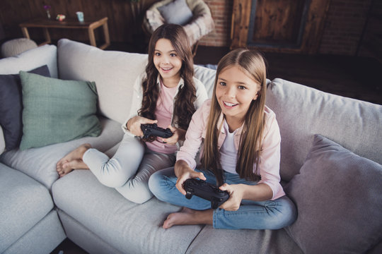 Above high angle view portrait of two nice lovely sweet attractive charming cheerful cheery positive girls sitting on divan playing video game battle crossed legs in house loft industrial interior