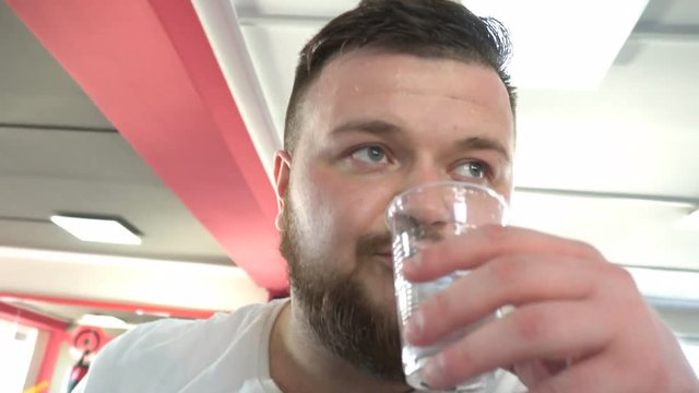 A man with a beard drinking water in the gym after a workout, the replacement of fluid in the body