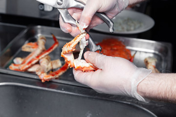 Cook chef is carving fresh red big boiled prepared blue kamchatka crab with scissors. Concept useful seafood in a menu, chef of premium restaurant preparing crab for serving for guests, clients
