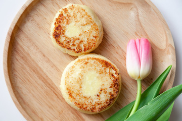 Closeup fresh flower pink tulip on wooden round plate, two golden fried cheesecakes in the shape of a figure 8, dessert made from cottage cheese. Concept tasty and healthy breakfast March 8
