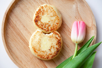 Closeup of fresh pink tulip on wooden round plate, two golden bitten fried cheesecakes in the shape of figure 8, dessert made from cottage cheese. Concept tasty and healthy breakfast March 8