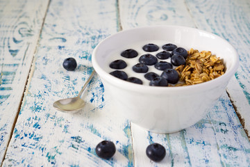 Oat granola with blueberries and yogurt in a bowl on a white and blue rustic background with copy space