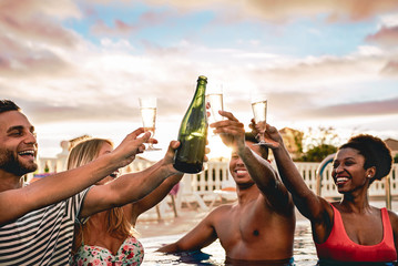 Happy friends doing pool party toasting champagne at sunset - Young people having fun drinking...