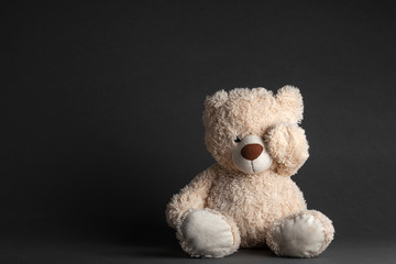 a little bear sits in a black room on a chair with his eyes closed hands