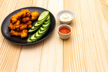 Chicken fried (nuggets) homemade on black plate with two sauces - mayonnaise and hot spicy sauce. On wooden background