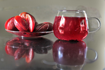 Plums in a saucer and a cup of juice on the table