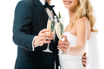 selective focus of bride and groom clinking glasses of champagne isolated on white