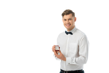 smiling groom holding gift box with wedding ring and looking at camera isolated on white