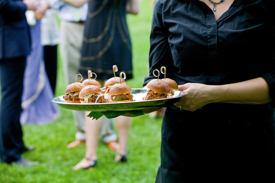 a server holding a tray full of mini pulled pork sandwiches during a catered event