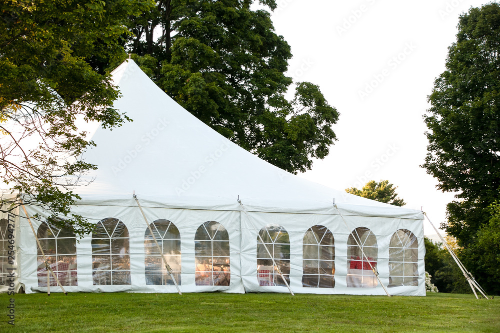 Wall mural a white wedding tent set up in a lawn surrounded by trees and with the sides down