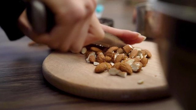 Close-up of femal hands cutting and crunching almonds on a wooden cutting board