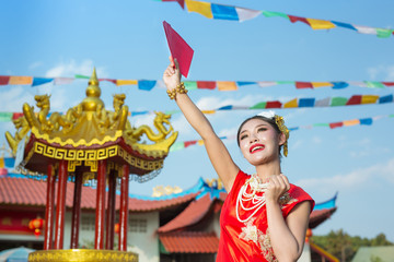 A beautiful asian girl wearing a red dress holding paper fan in her hand and smiling makes her look happy.