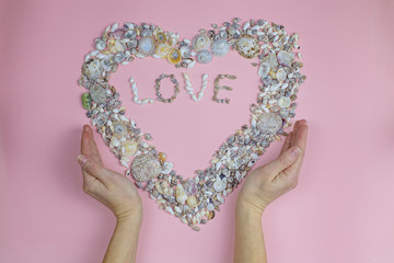Hands hold the word love and a heart lined with seashells. Love concept