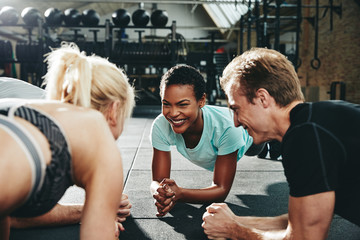 Smiling friends planking together during a gym workout class