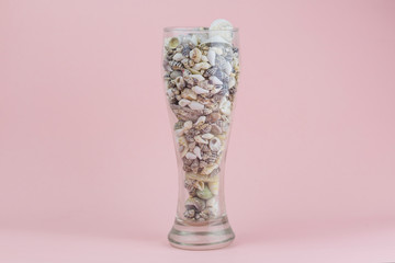 Transparent vessel filled with seashells on pink background. The concept of summer vacation