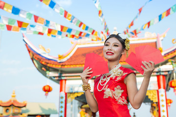A beautiful asian girl wearing a red dress holding paper fan in her hand and smiling makes her look happy.