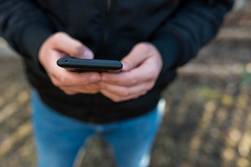 Young man wearing jeans using a modern smartphone with rubber case, focus on the phone.