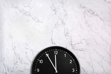Black wall clock on white marble texture. Office clock on marble background