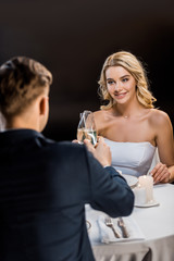 selective focus of beautiful bride and groom clinking glasses of champagne on black background