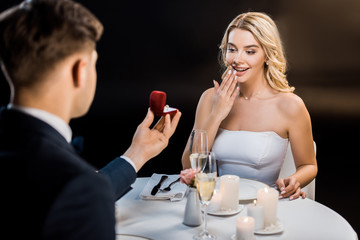 selective focus of man making marriage proposal to amused woman on black background